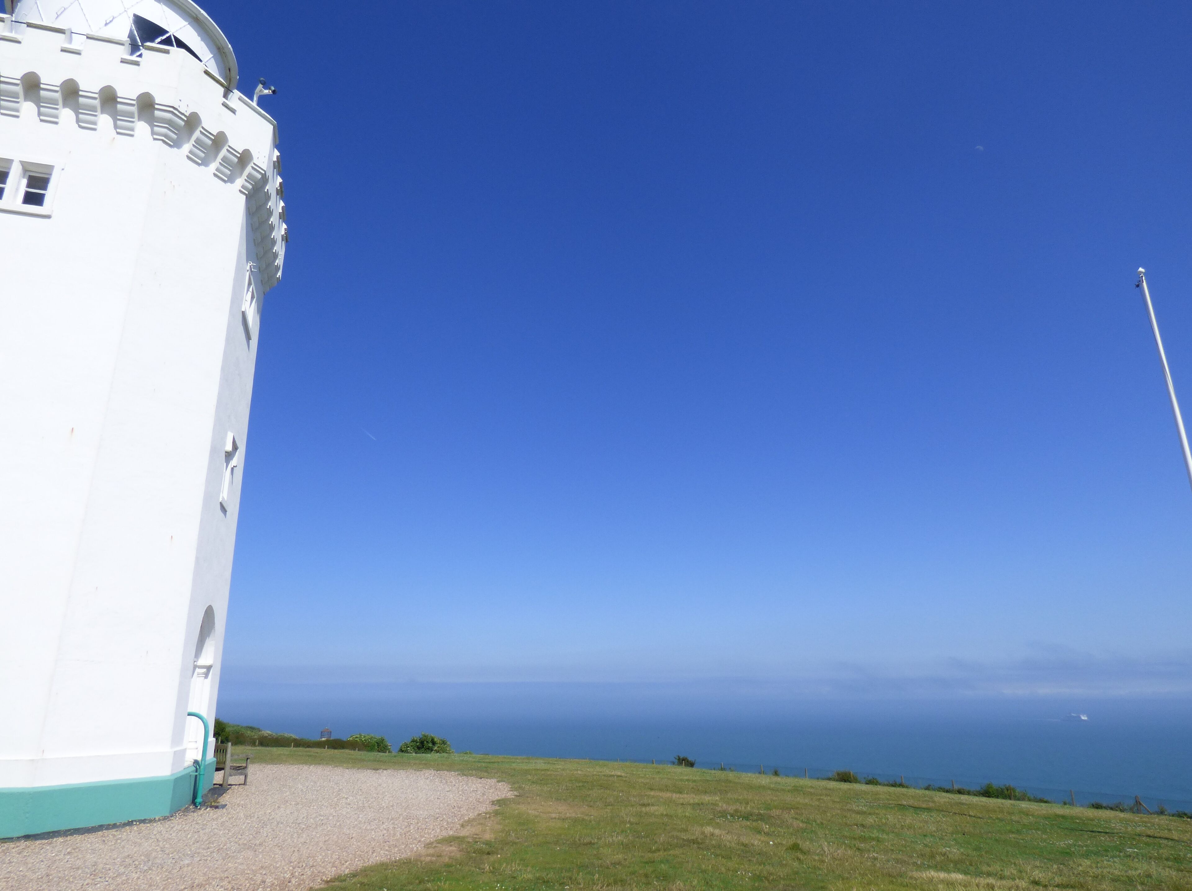 Um farol branco com vista ampla do oceano e céu claro.