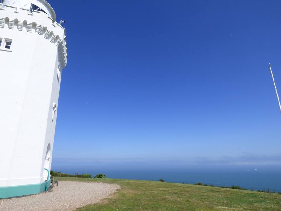 Um farol branco com vista ampla do oceano e céu claro.