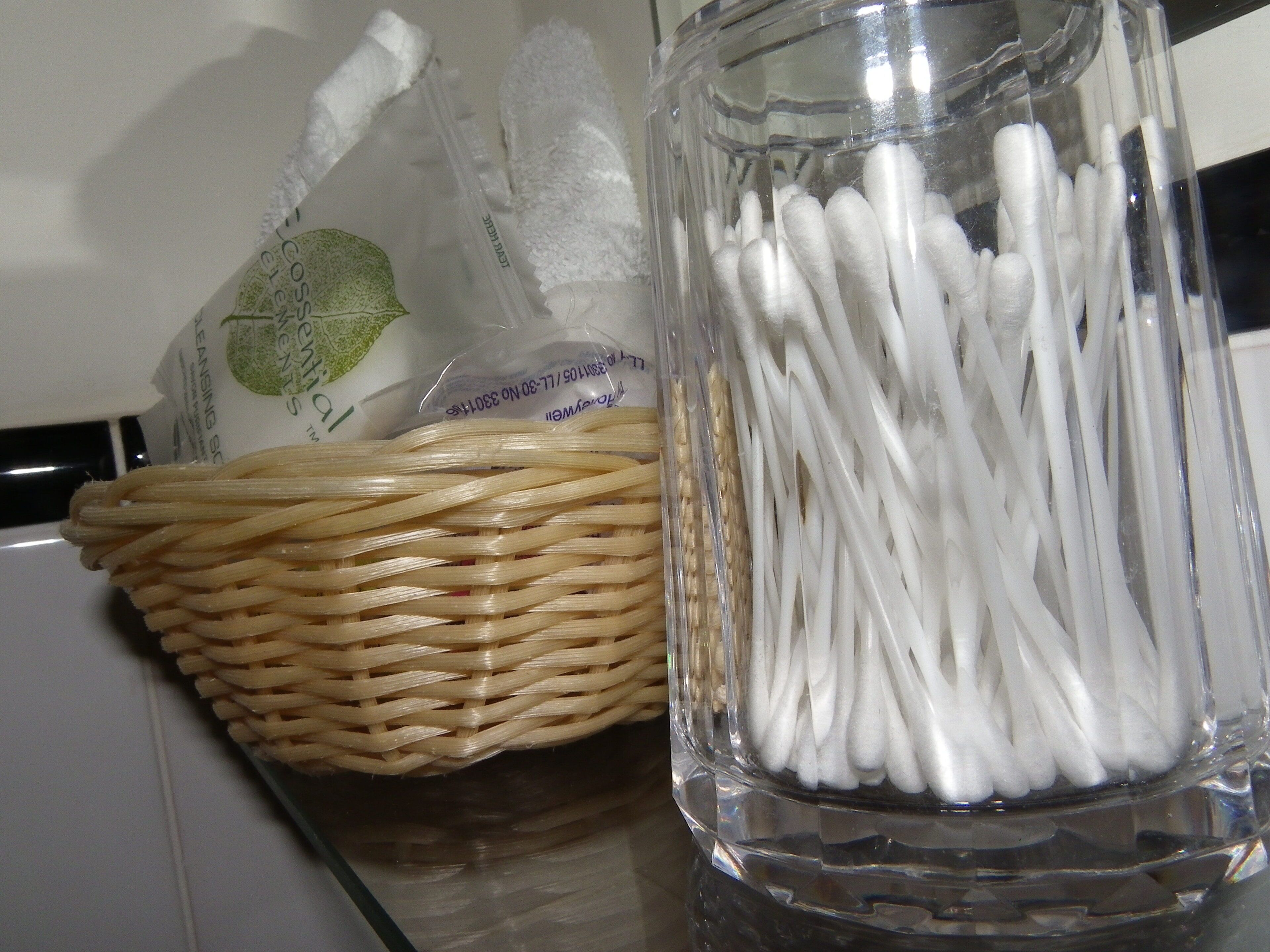 A woven basket and a glass jar filled with white cotton swabs.