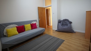 Una sala de estar con un sofá gris, un sillón de peluche gris y una puerta de madera que da a otra habitación.