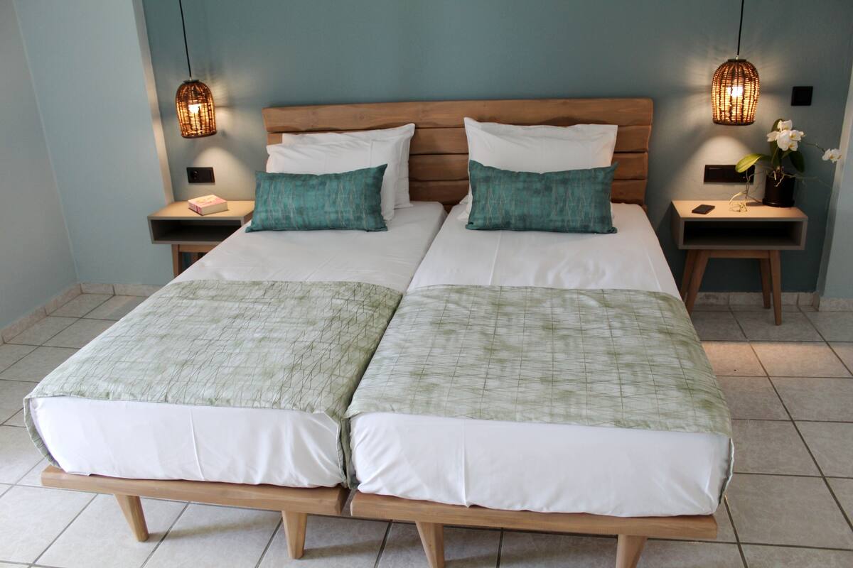 A double bed with a wooden frame, two nightstands with wicker lamps, and a small table with a vase of flowers.