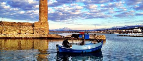 A lighthouse and a small boat in a harbor with a stone wall and distant mountains.