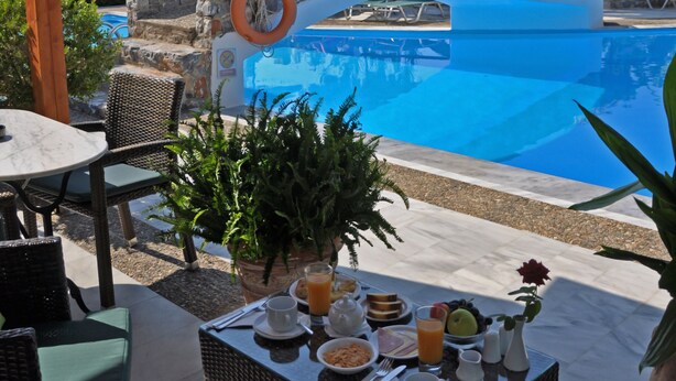 A pool area with a stone bridge, wicker furniture, and a table set with breakfast. - Poledas Apartments (Apokoronas)