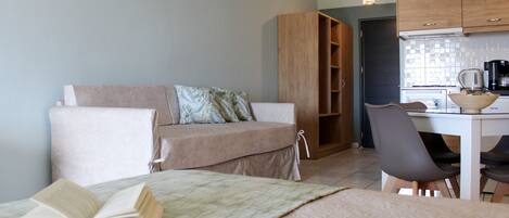 A cozy living area with a sofa, a dining table with chairs, and a kitchen area with cabinets and appliances.
