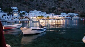 A coastal village with white buildings, boats docked in the water, and a rocky hillside in the background. - Poledas Apartments (Apokoronas)