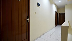A hallway with a wooden door, a white wall, and a tiled floor. - ZEN Rooms Kampung Bali Tanah Abang (Jakarta)