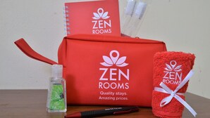 A red bag with the logo 'ZEN ROOMS' and a notebook, a bottle of hand gel, a pen, and a red towel tied with a white ribbon. - ZEN Rooms Kampung Bali Tanah Abang (Jakarta)