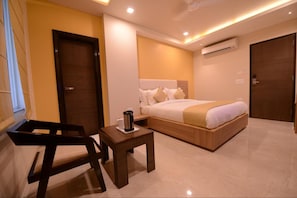 Quarto de hotel com uma cama, uma mesinha com cafeteira e uma cadeira.