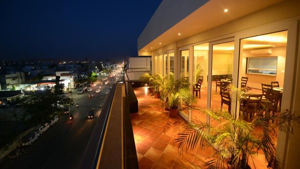 Vista noturna de um hotel com varanda e vista para uma rua movimentada.