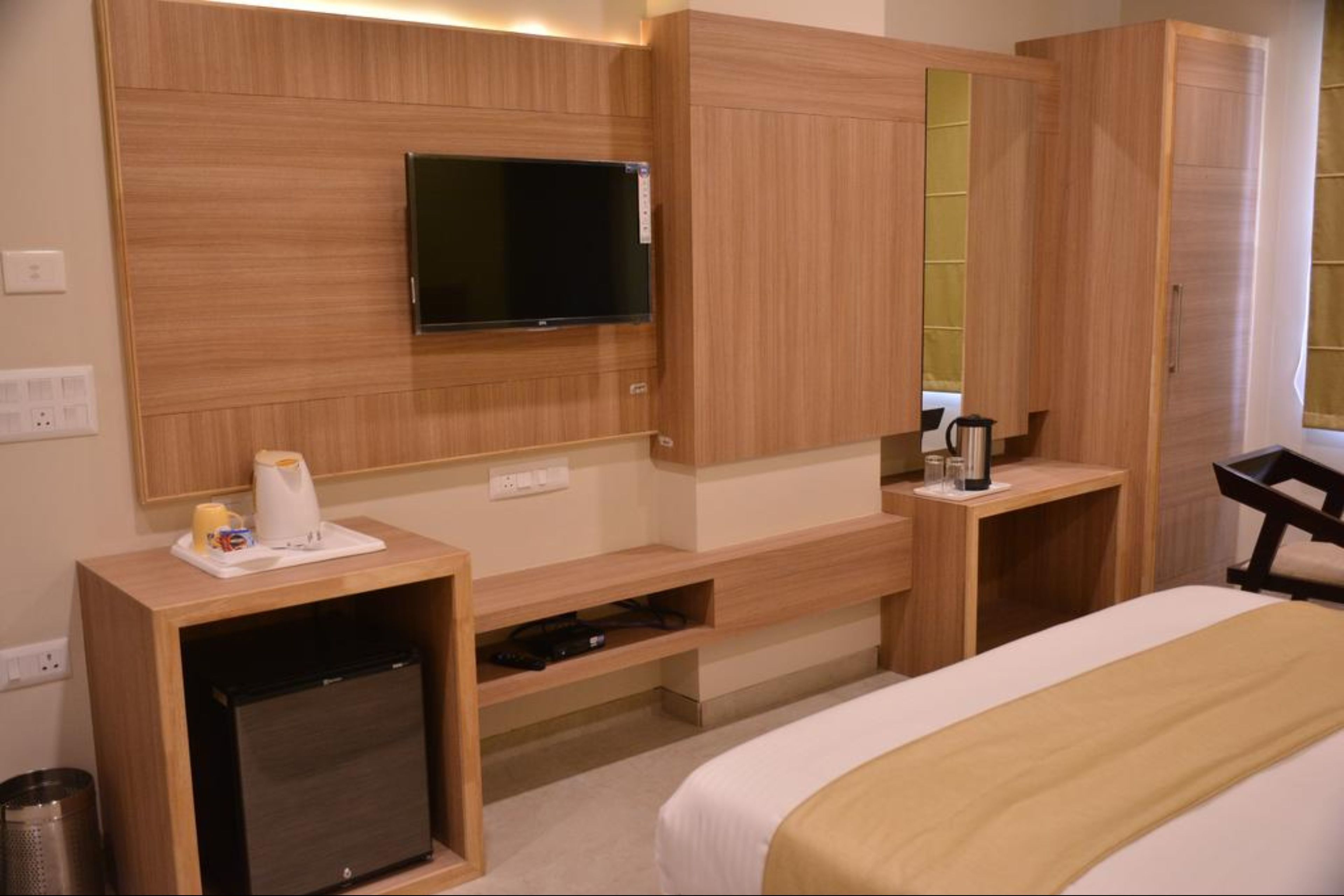 Een hotelkamer met een bed, een aan de muur bevestigde televisie, een klein bureau met een koffiezetapparaat en een kledingkast.