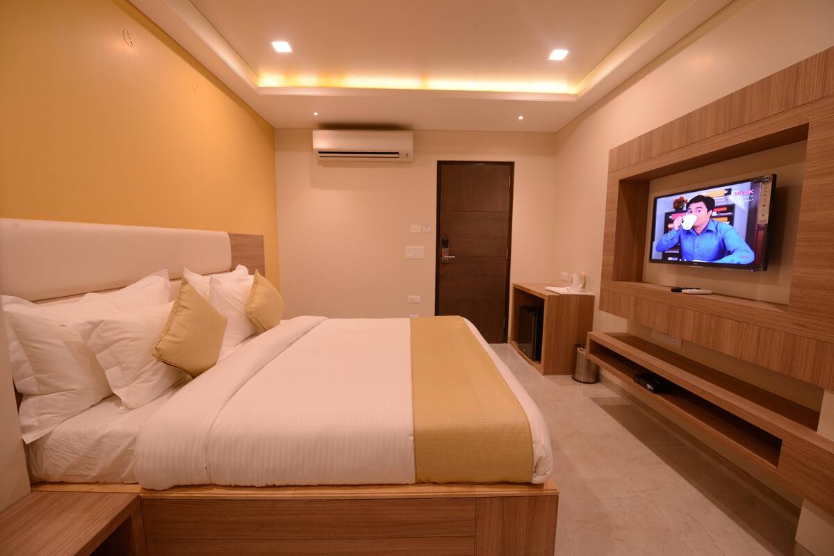 A modern hotel room with a neatly made bed, a television mounted on the wall, and a wooden nightstand.