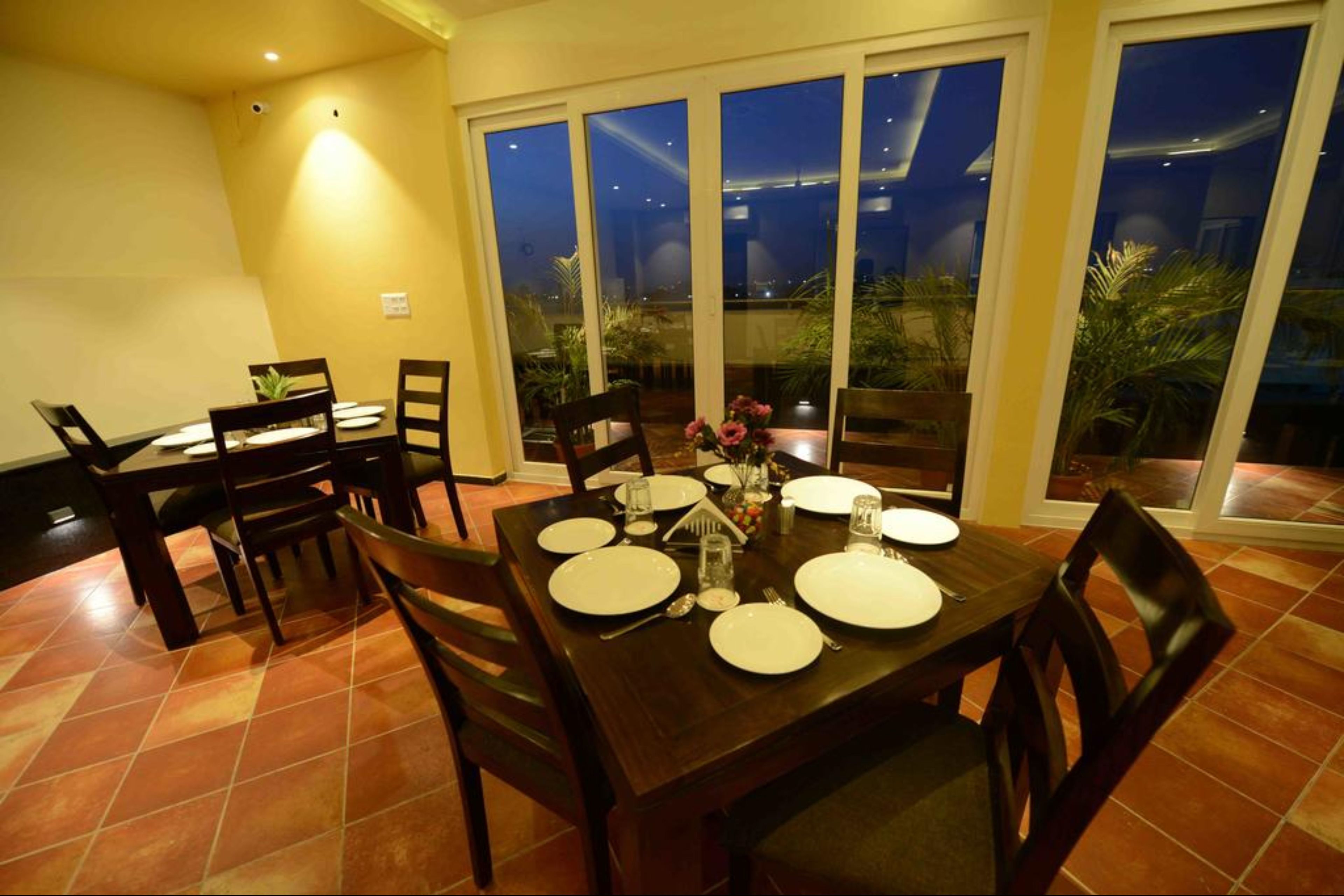 A dining area with a table set for four, surrounded by chairs, and large windows offering a view of the outdoors.