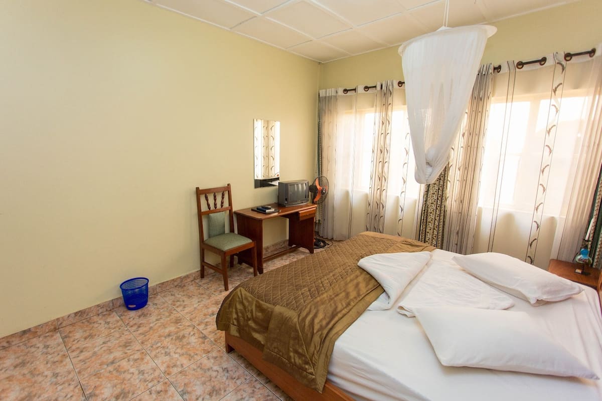 A hotel room with a bed, a desk, a chair, a television, and a mosquito net.