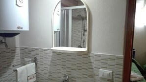 A bathroom with a white sink, a mirror with an integrated shelf, and a shower visible in the background. - Anita's House in the Heart of Segesta CIN IT081003C2BTVOXQJS  (Calatafimi)