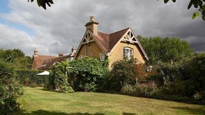 Une maison traditionnelle, dotée d’un toit à forte pente, entourée d’un jardin bien entretenu et d’arbres majestueux.