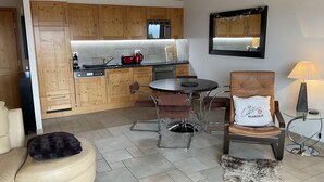 A modern kitchen with wooden cabinets, a dining area with a round table and chairs, a sofa, and a fur rug.