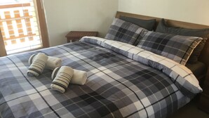A bed with a checkered bedspread, two rolled-up towels, and a wooden nightstand beside it.