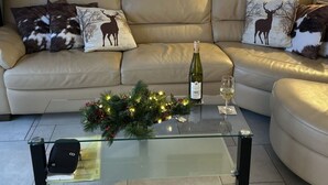 A living room with a beige leather sofa, two deer-themed pillows, a glass coffee table with a wine bottle and glass, and a small Christmas tree with lights. - NENDAZ 4-VALLEES  2 Bedroom Apartment with Indoor Swimming Pool. (Haute-Nendaz)