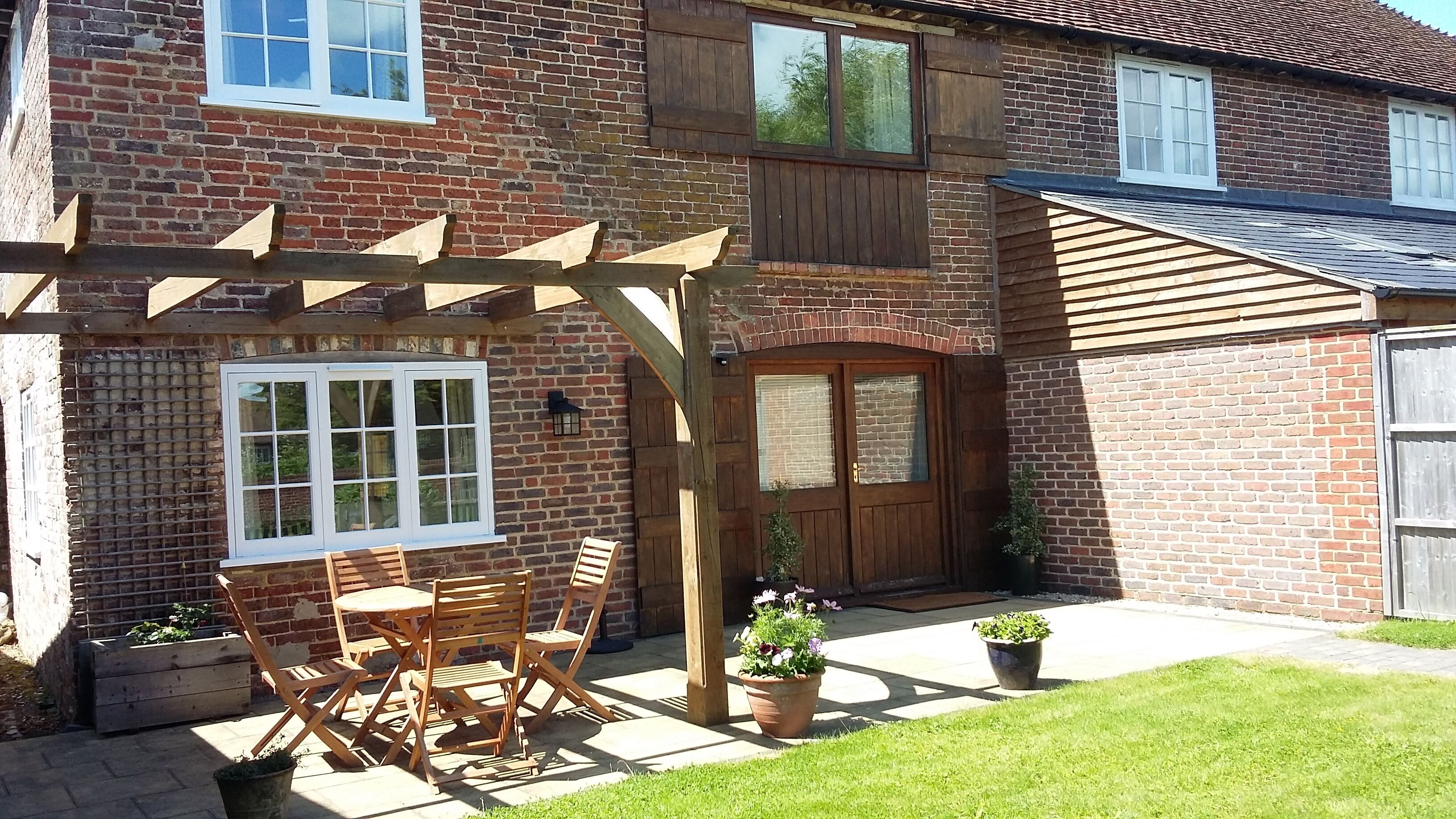 Una casa de ladrillo con una pérgola de madera, una puerta principal y un pequeño patio con mesa y sillas.
