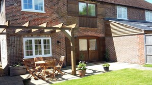 Una casa de ladrillo con una pérgola de madera, una puerta principal y un pequeño patio con mesa y sillas.