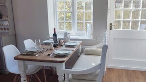 Un comedor con mesa de madera dispuesta para cuatro personas, sillas blancas y ventana con vista a árboles.