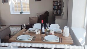 Comedor con mesa de madera dispuesta para cuatro personas, incluyendo platos, vasos, cubiertos y una botella de vino.