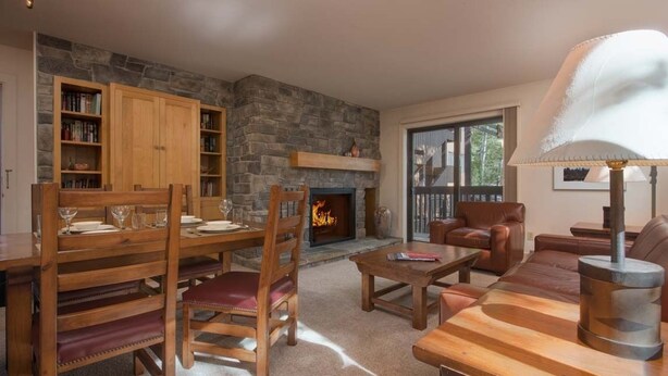 A cozy living room with a stone fireplace, wooden furniture, and a bookshelf. - JHRL - Sleeping Indian West #10 (Teton Village)