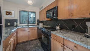 A kitchen with wooden cabinets, a black microwave, a stove, and a window with a view. - JHRL - Sleeping Indian West #10 (Teton Village)