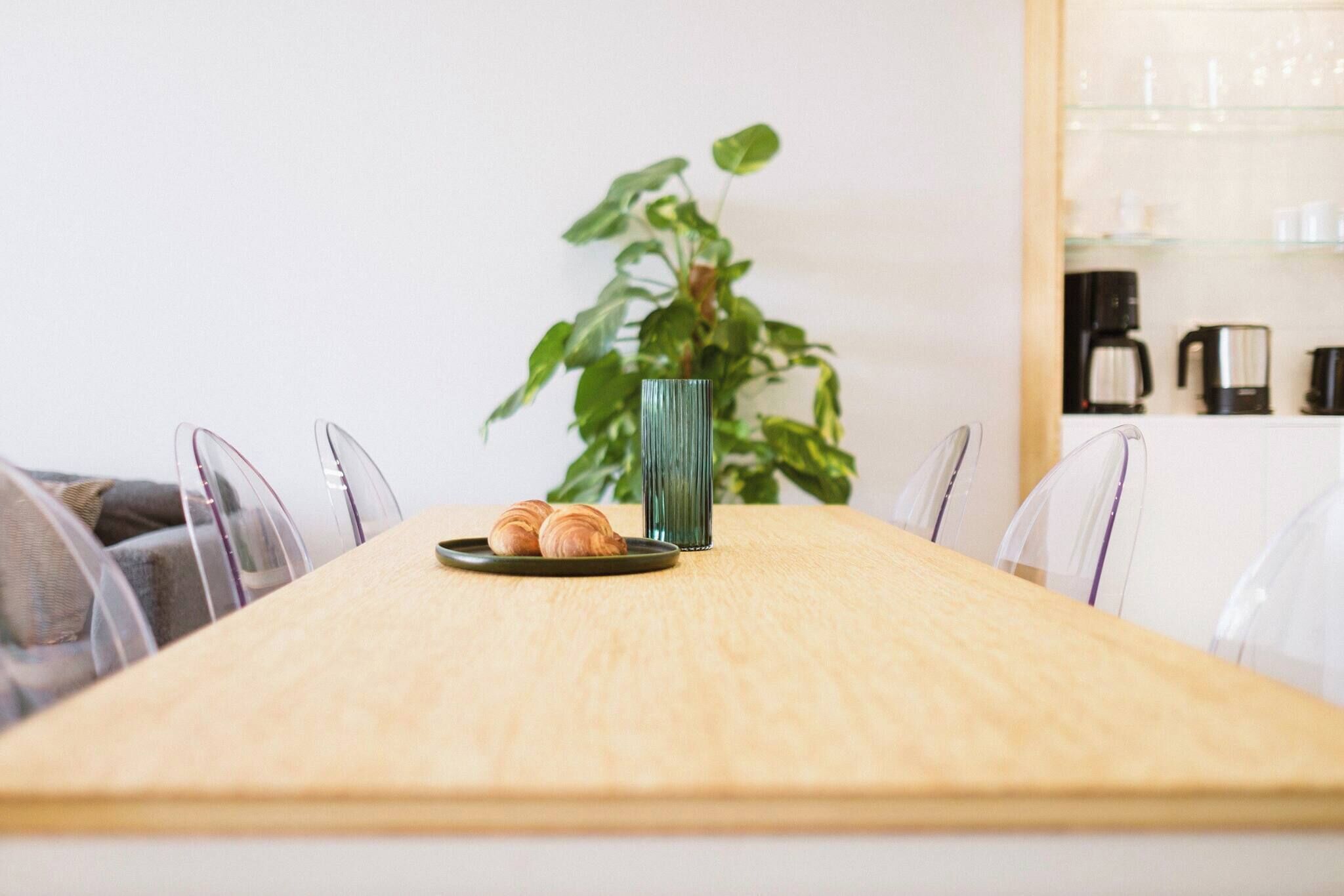 Ein Holztisch mit einer Schüssel Croissants und einer hohen, grünen Vase.