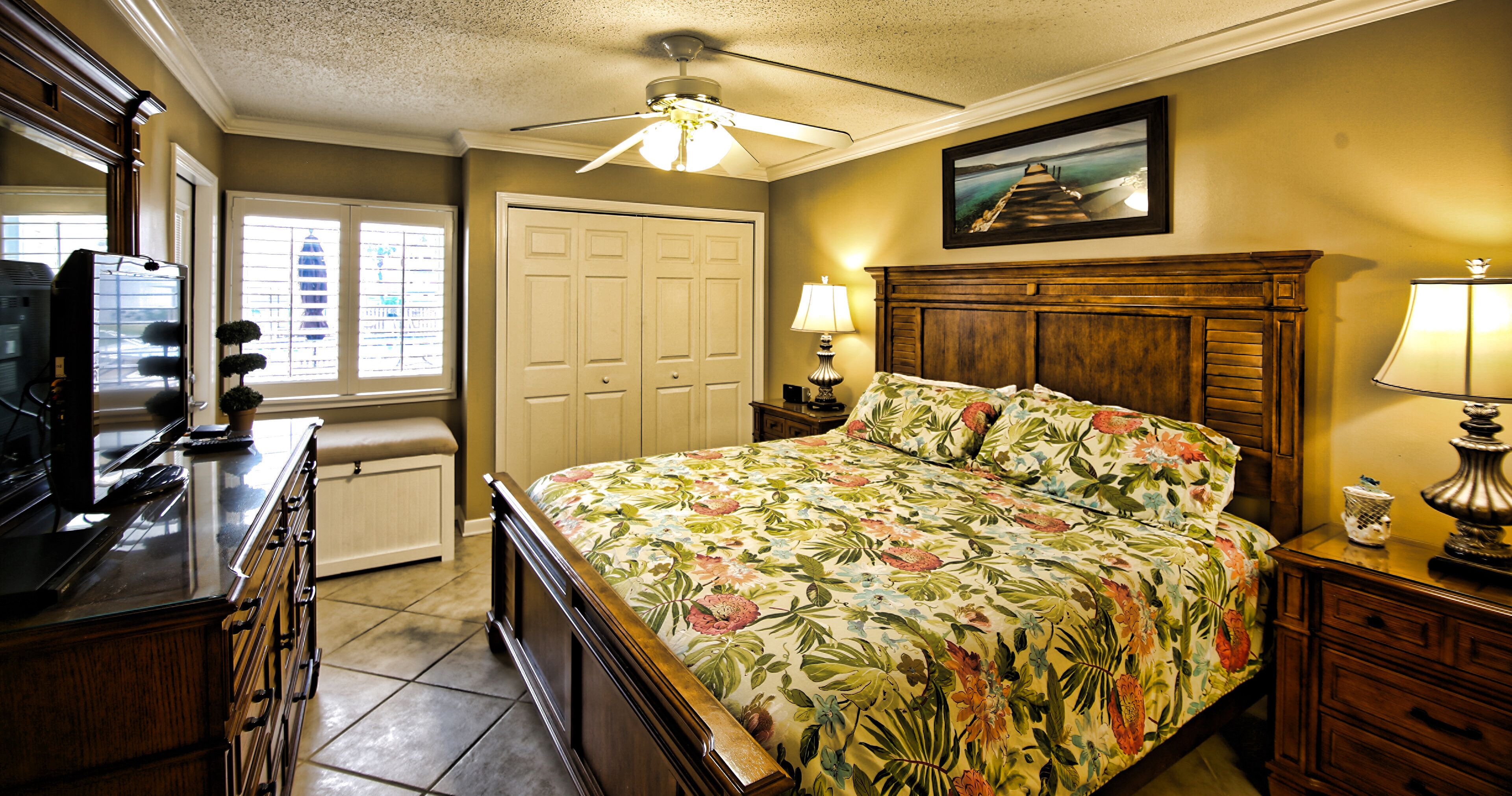A bedroom with a bed, a nightstand, a dresser, a ceiling fan, and a window with blinds.