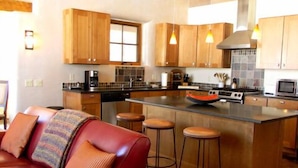 A modern kitchen with wooden cabinets, a central island with stools, and a red leather sofa in a living area.