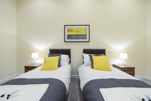 Une chambre d’hôtel avec deux lits, chacun étant doté d’une table de chevet, d’une lampe et d’un tableau encadré au mur.