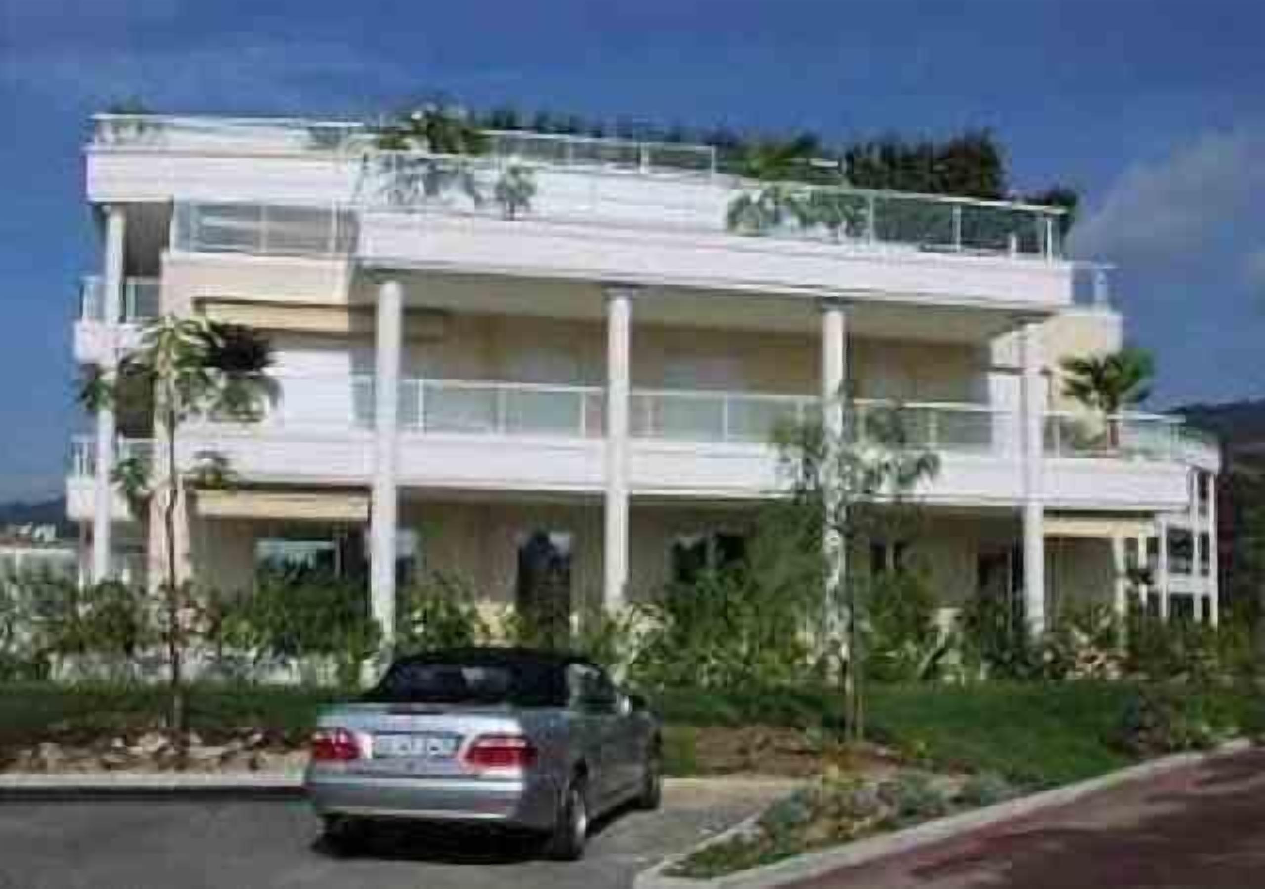 A multi-story building with balconies and a car parked in front.
