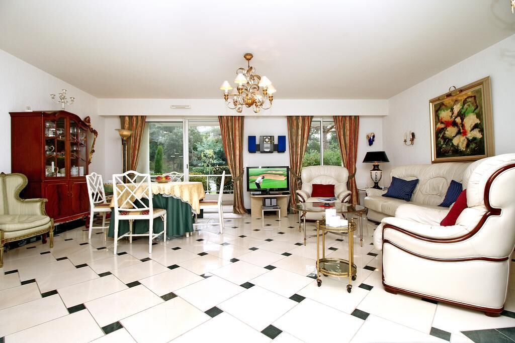 A living room with a television, a sofa, a dining table with chairs, a chandelier, and a cabinet.