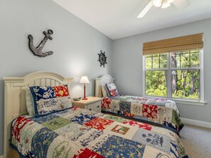 Une chambre avec deux lits, une fenêtre donnant sur la verdure et des éléments décoratifs fixés au mur.