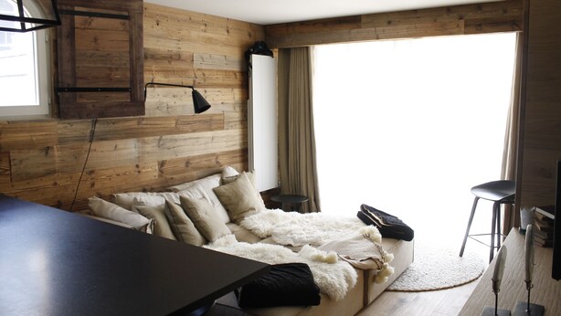 Ein modernes Schlafzimmer mit einer Holzwand, einem großen Bett mit vielen Kissen, einem kleinen runden Tisch und einem Stuhl.