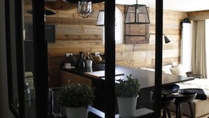 Eine moderne Küche mit Holzakzenten, eine Essecke mit Hockern und ein gemütlicher Wohnbereich mit Sofa und großem Fenster.