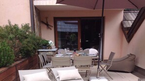 Eine Terrasse mit vier Liegestühlen, einem Tisch und Stühlen sowie einem großen Sonnenschirm.