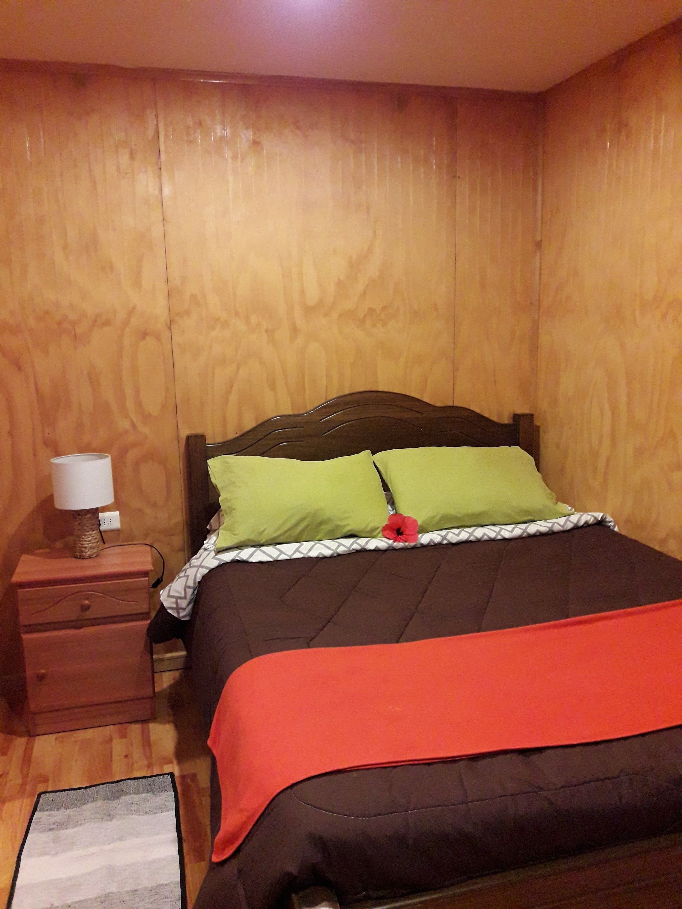 A bedroom with a wooden headboard, a nightstand with a lamp, and a bed with green and red bedding.