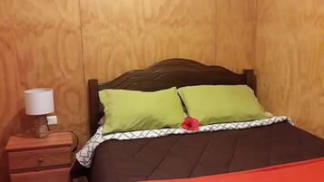 A bedroom with a wooden headboard, a nightstand with a lamp, and a bed with green and red bedding.