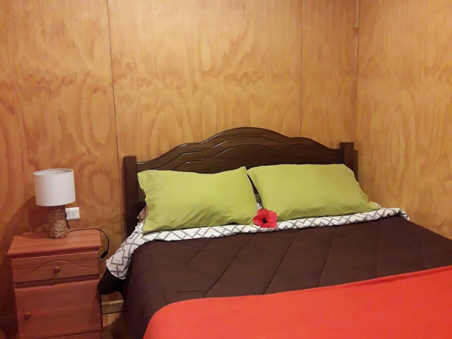 A bedroom with a wooden headboard, a nightstand with a lamp, and a bed with green and red bedding.