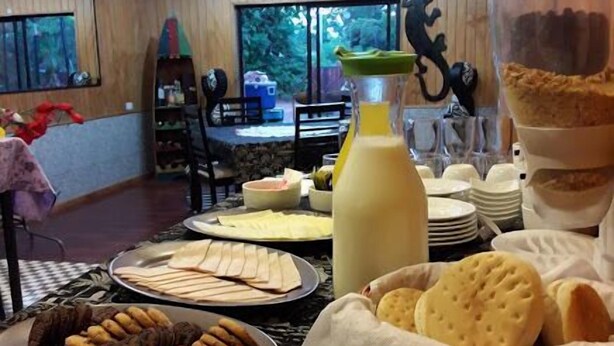 A dining area with a table set for breakfast, including plates of food, a bottle of juice, and a pitcher. - La Casa del Kori - Hostal - Hostel (Hanga Roa)