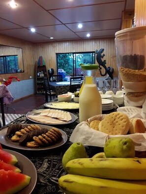 A dining area with a table set for breakfast, including plates of food, a bottle of juice, and a pitcher. - La Casa del Kori - Hostal - Hostel (Hanga Roa)