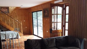 A living room with a dark brown leather sofa, a glass coffee table with candles, a wooden staircase, and a dining area with a table and chairs. - La Casa del Kori - Hostal - Hostel (Hanga Roa)