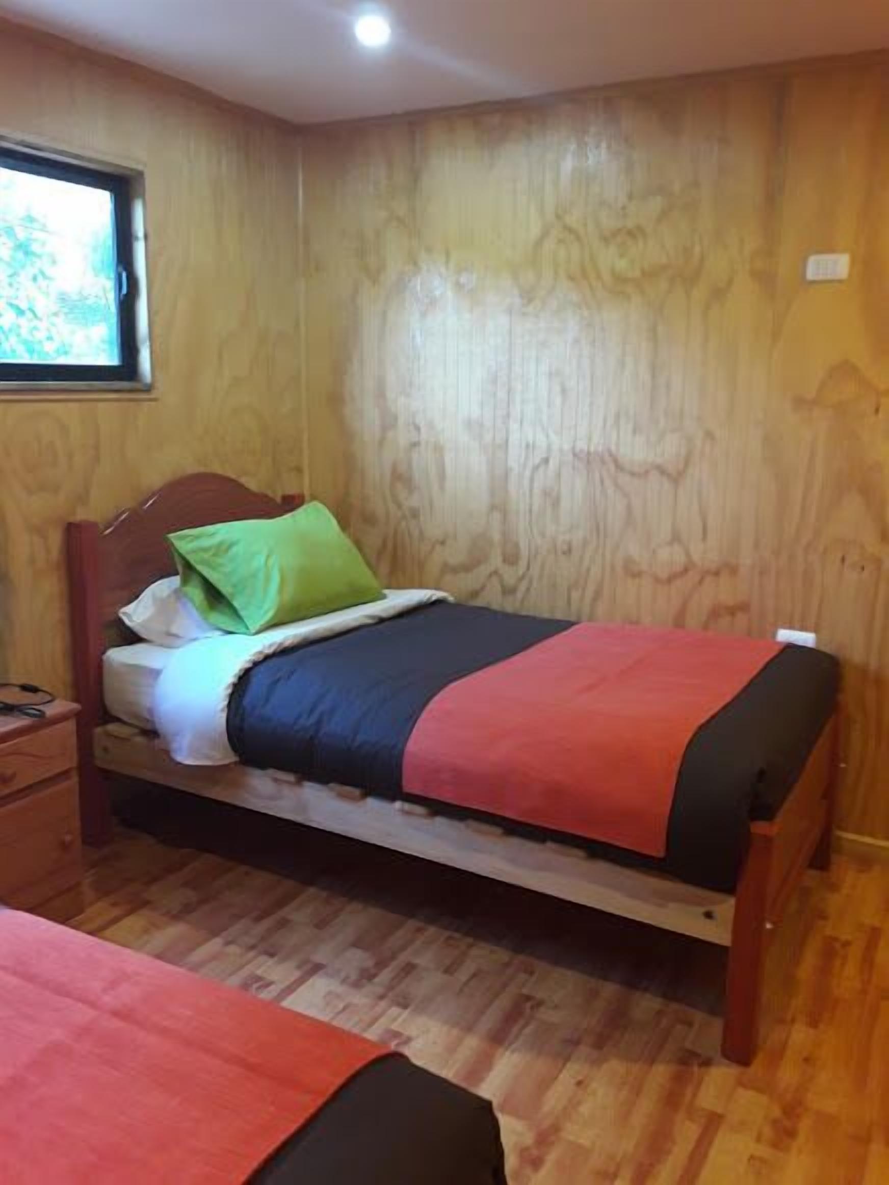 A single bed with a wooden headboard, a green pillow, and a red blanket.