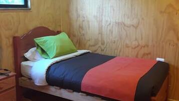 A single bed with a wooden headboard, a green pillow, and a red blanket.