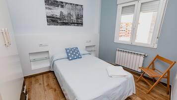 A bedroom with a bed, a window, a radiator, and a chair.