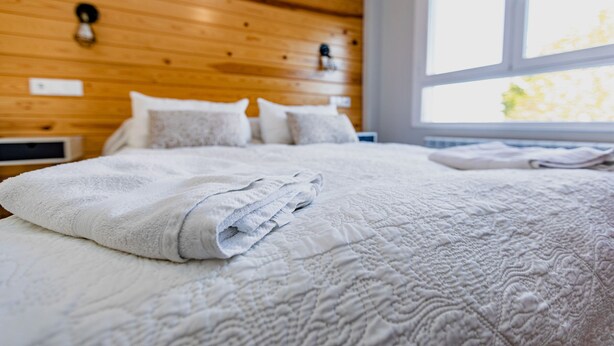 Una cama bien hecha con una colcha blanca acolchada y almohadas, un cabecero de madera y una ventana con luz diurna.