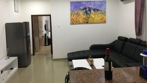 Un soggiorno moderno con un divano scuro, un angolo cottura con frigorifero e un quadro appeso al muro.
