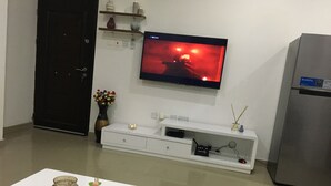 Un soggiorno moderno con una TV a schermo piatto montata a parete, un mobile bianco per l'elettronica sottostante, un armadietto nero e un frigorifero.